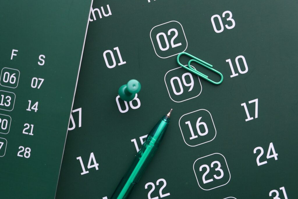 Close-up of a green calendar with pen, push pin, and paper clip for planning and organization.